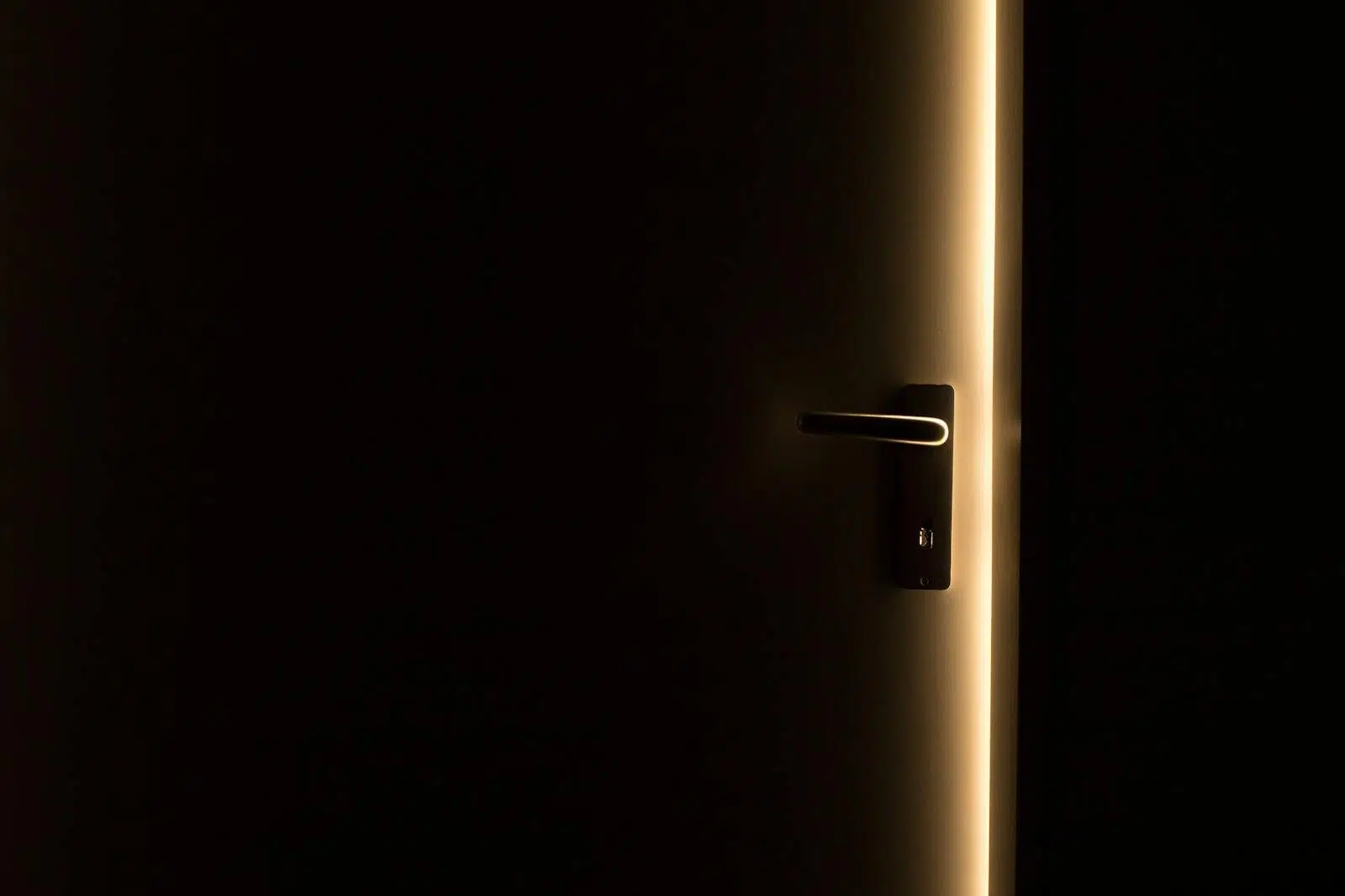 A dark room with a door slightly ajar, revealing a glowing light through the opening.